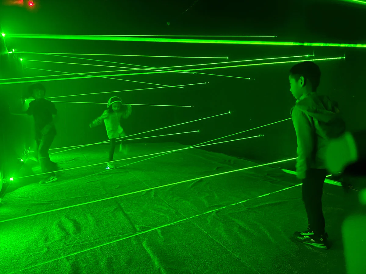Kids play in an activity room with green lighted laser maze.