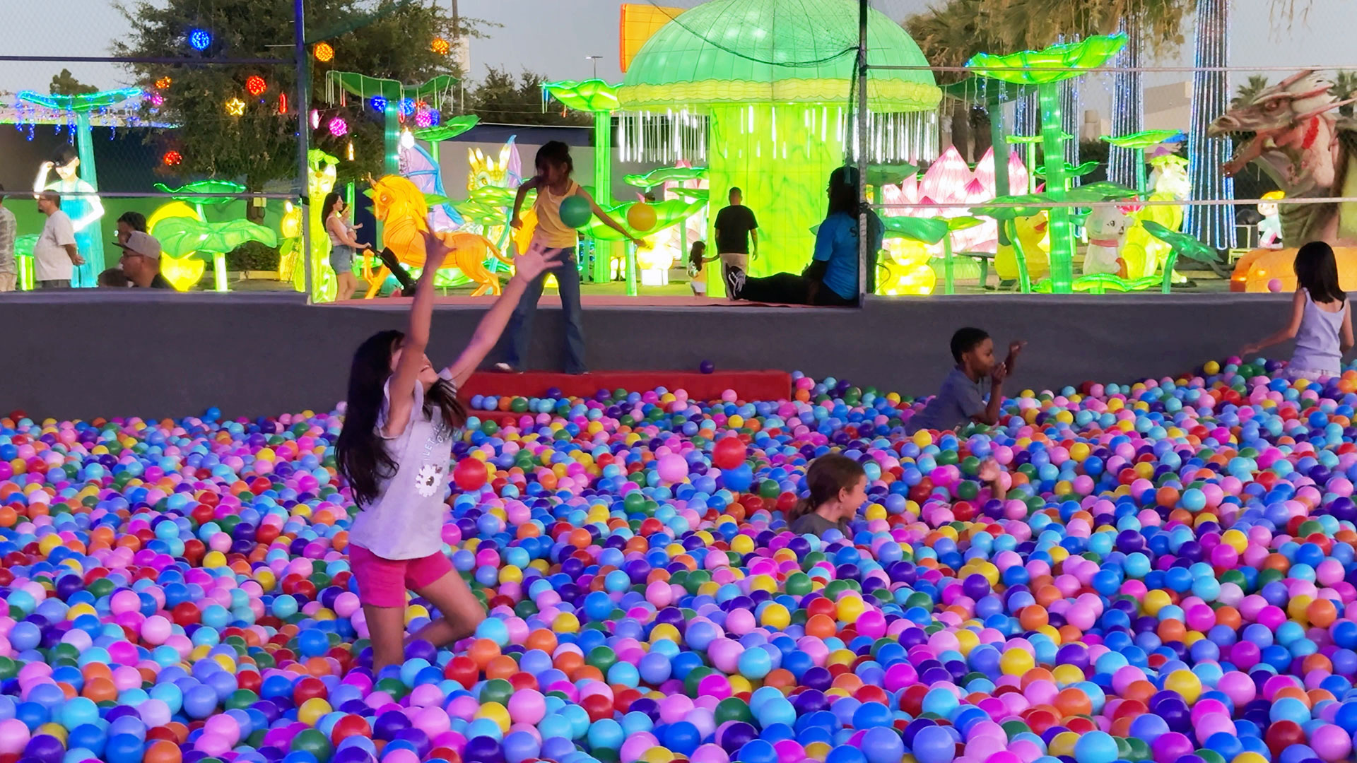 Four kids playing in a ball pit with lighted structures in the background