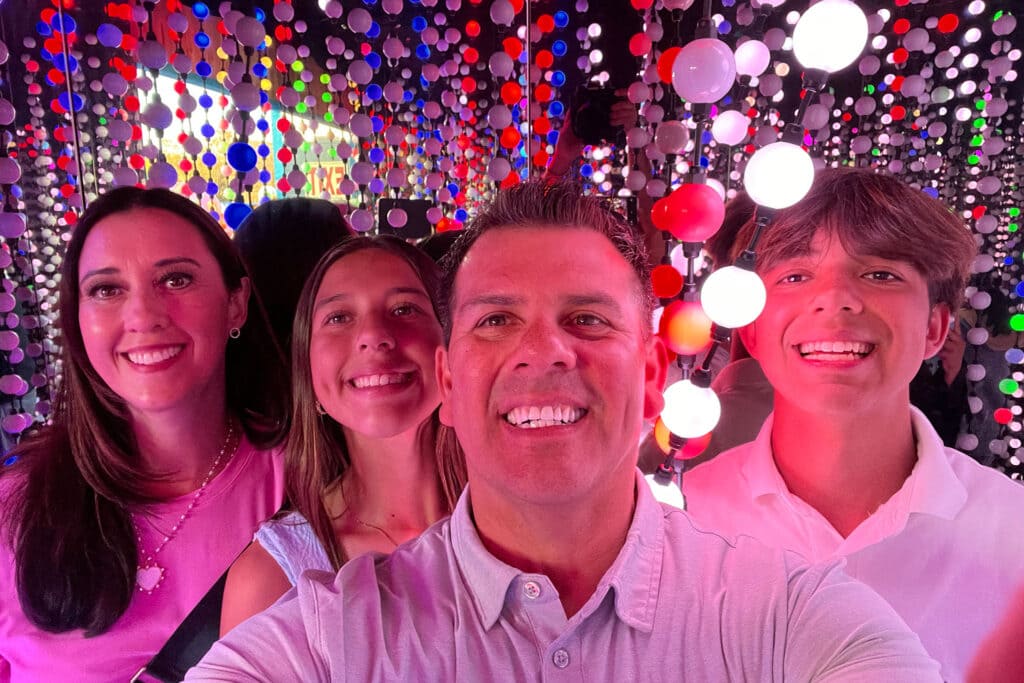 A family of four smiling for a selfie with hanging lights around them