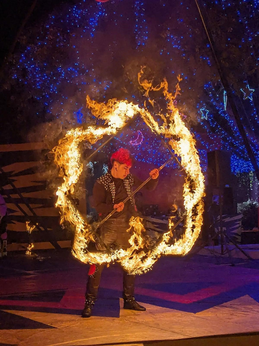 Circus performer in a red hat spins fire.