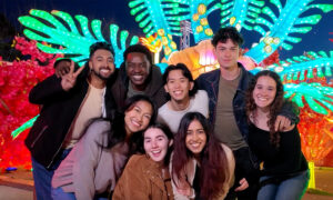 A group of young adults pose for a photo with a bright green lit structure behind them.