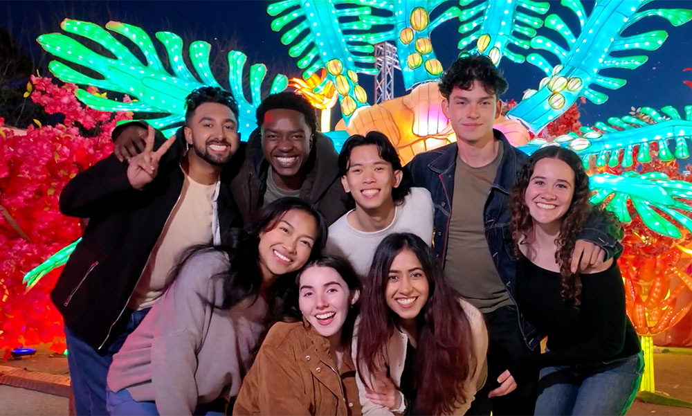 A group of young adults pose for a photo with a bright green lit structure behind them.