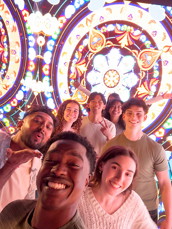 A group of young adults pose for a photo in an infinity mirror room.