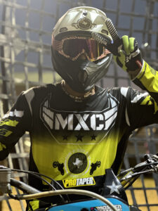 Imaginarium A motocross racer wearing a helmet, goggles, and a racing jersey with "MXC" logo adjusts his helmet before a race.